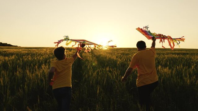 Son and dad run with kites on green field against sunset