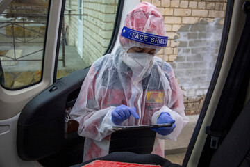 A paramedic girl, in an anti-virus suit, near the ambulance, fills the tablet.