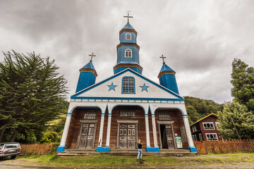 Holzkirche Nuestra Senora Del Patrocinio in Tenaun auf Chiloe mit weißer Fassade, blauen Sternen und Kirchtürmen sowie weißen Säulen im Eingangsbereich