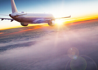 Fototapeta premium Passengers commercial airplane flying above clouds in sunset light. Concept of fast travel, holidays and business.