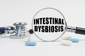 On a white surface lie pills, a stethoscope and a magnifying glass with the inscription - INTESTINAL DYSBIOSIS