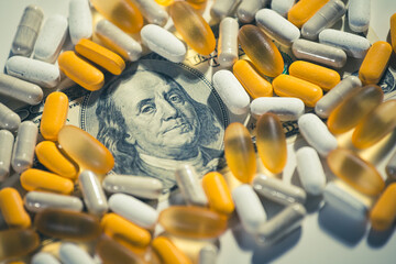 Big pharma conspiracy theory. Medical pills lying on top of hundred of US Dollar Bill. Pharmacy and...
