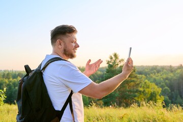 Middle aged bearded man with smartphone backpack on hike, making video call