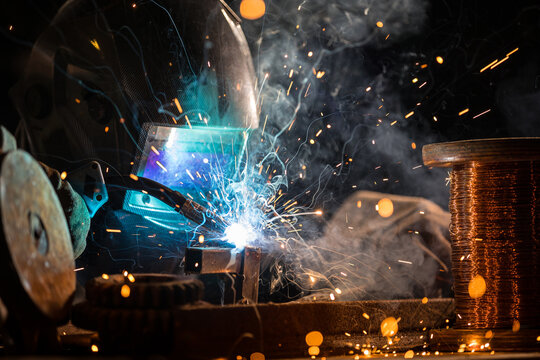 Welder welding a piece of iron tool in a factory