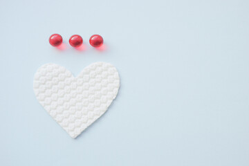 Three red vitamins and white heart on pale blue table. Copy space