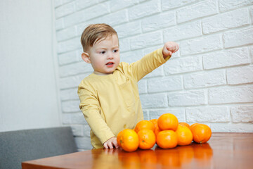 A little boy 2 years old is standing at a table with tangerines. Baby wants to sit down citrus fruits for the first time