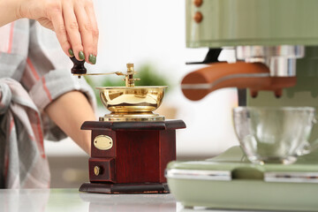 Woman grinding coffee and modern coffee machine on table in kitchen