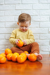 Little boy 2 years old eats tangerines. The kid wants to sit on citrus fruits for the first time. Healthy fruits for children