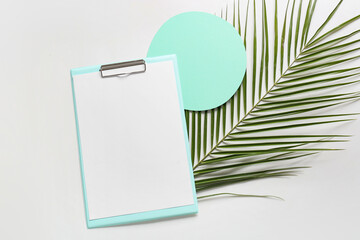 Clipboard with blank sheet of paper and palm leaf on white background