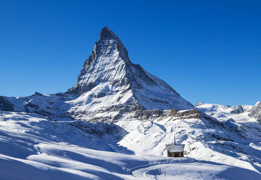 The small Riffelberg chapel Brother Klaus stands on the snow-covered hill with the giant Alps sumit Matterhorn at the background.