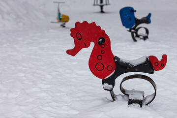 children's swing in the form of a seahorse on the playground in winter