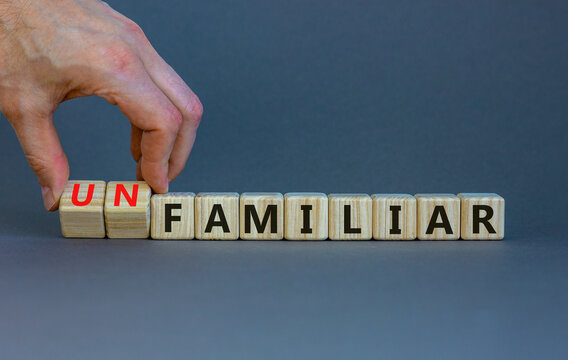Familiar or unfamiliar symbol. Businessman turns wooden cubes changes the word unfamiliar to familiar. Beautiful grey table grey background, copy space. Business, familiar or unfamiliar concept.