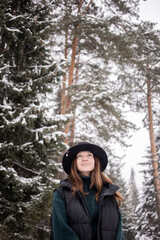 Young caucasian woman in black hat in winter snowy forest. 