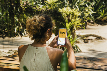 Girl in the park holding a smartphone with Taxi Service app on the screen. Rustic wooden table....