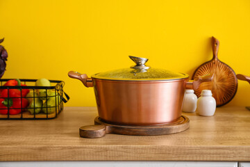 Wooden board with cooking pot on table near color wall