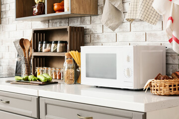 Counter with microwave oven and food near light brick wall in kitchen