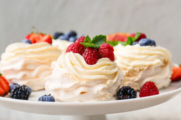 Stand with tasty Pavlova cakes and fresh berries on table, closeup