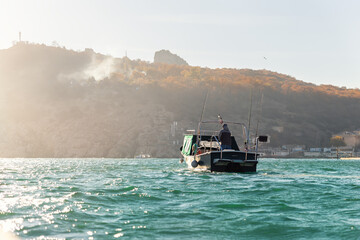 Scenic back view of fisherman angler enjoy fishing with rods on motor boat ship at clean green blue...
