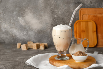 Board with glass of tasty iced hojicha latte, milk and powder on grey background