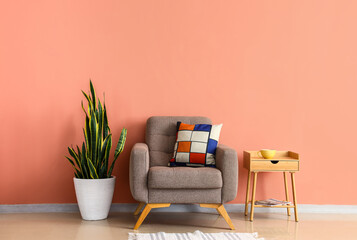 Wooden table with cup, soft armchair and houseplant near pink wall