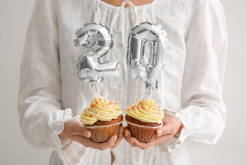 Woman holding Birthday cupcakes with number 20 on light background