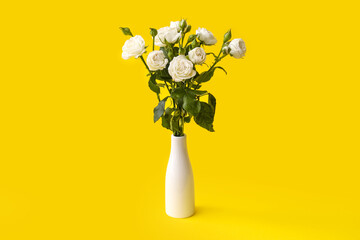 Vase with bouquet of beautiful roses on yellow background