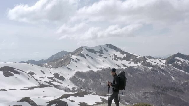 Adventurous hiker standing on mountain peak admiring snow covered mountains
