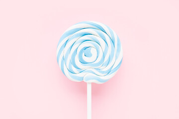 Blue-white lollipop on a white stick on a light pink background. Top view, copy space