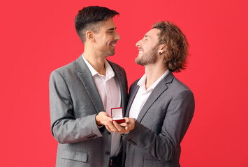 Happy engaged gay couple on red background
