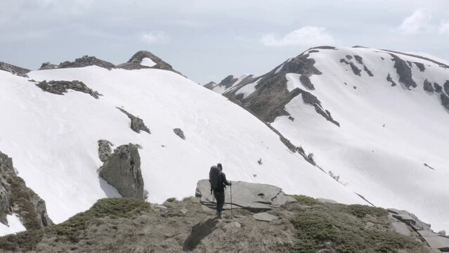 Hiker approaching rocky peak with a view on mountain range covered in snow