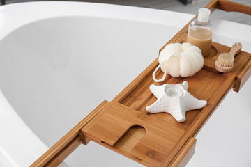 Wooden tray with accessories and candle on bathtub, closeup