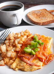 Omelette with cheese, red tomato and onion spicy salsa and cubes of green peppers on top with a side of squared deep fried potatoes black coffee and toasted bread side view macro photography. Vertical