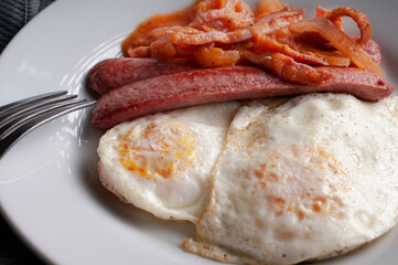 Macro photography well done fried eggs with sausage and tomato and onion spicy salsa on a white plate with a fork on the side 