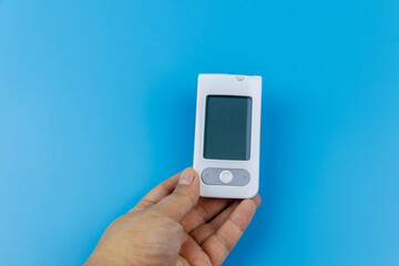 Digital glucometer in female hand over a pastel blue background. Diabetes concept
