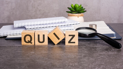 the word Quiz is written on wooden cubes on a gray background. close-up of wooden elements, magnifying glass, paper documents