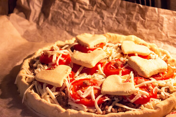 Festive homemade pizza with meat, tomatoes and cheese decorated with dough hearts. Romantic Valentine's Day dinner. Do-it-yourself pizza for Valentine's Day is baked in the oven. High quality photo