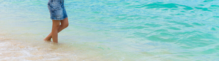 A young woman stands barefoot on the sandy seashore.