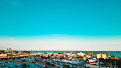 A clean blue sky with some small buildings and the ocean behind.