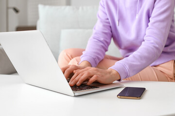 Young woman with modern laptop and mobile phone at home
