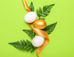 Composition with beautiful Easter eggs, ribbon and fern leaves on green background