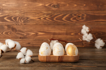 Holder with beautiful Easter eggs and cotton flowers on wooden background