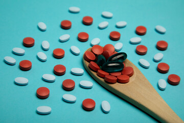 Studio photo of wooden spoon full of medical pills. There are red and light blue pills surrounding the spoon.