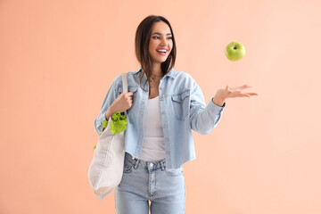 Young woman with eco bag and apple on beige background