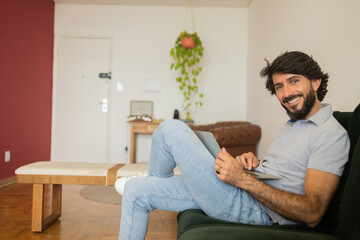Fototapeta premium Young business man working at home from his living room couch with laptop on his lap. Home office concept.