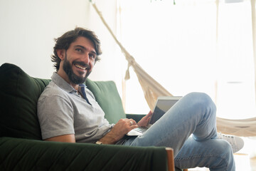 Young business man working at home from his living room couch with laptop on his lap. Home office concept.