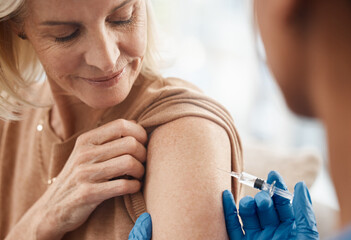 Life is slowly returning to normal. Shot of a doctor giving a senior woman an injection at home.