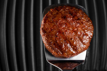 Meat steak on barbecue grilling tool - spatula handle. Cooking beef or pork patty. Raw cutlet for burger. Close-up photo.