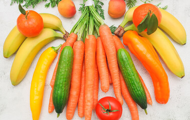 Seasonal vegetables and fruits: carrots, peppers, tomatoes, bananas, tangerines and apricots lie on a marble table.
