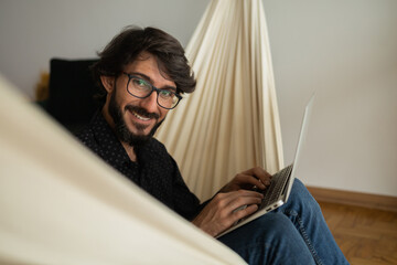 Young business man with black glasses working at home with laptop on a white hammock Home office concept.