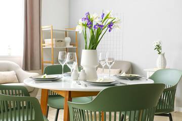 Table with setting and vase with iris flowers served for International Women's Day celebration in light room